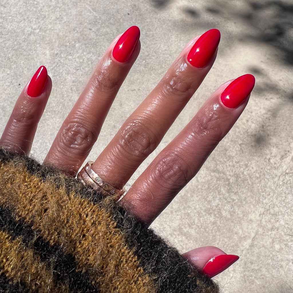 Hand with nails polished in vibrant scarlet red Smooch nail polish shown in natural sunlight for manicure display