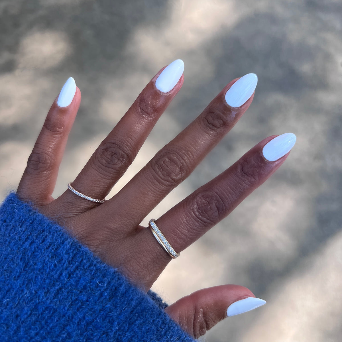 Hand with nails painted in smooth white Swan quick dry polish wearing delicate rings and cozy blue sweater outdoors