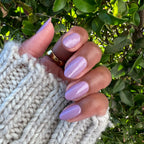 Hand with nails painted in glossy Prairie polish showing a soft blooming purple manicure by Olive and June