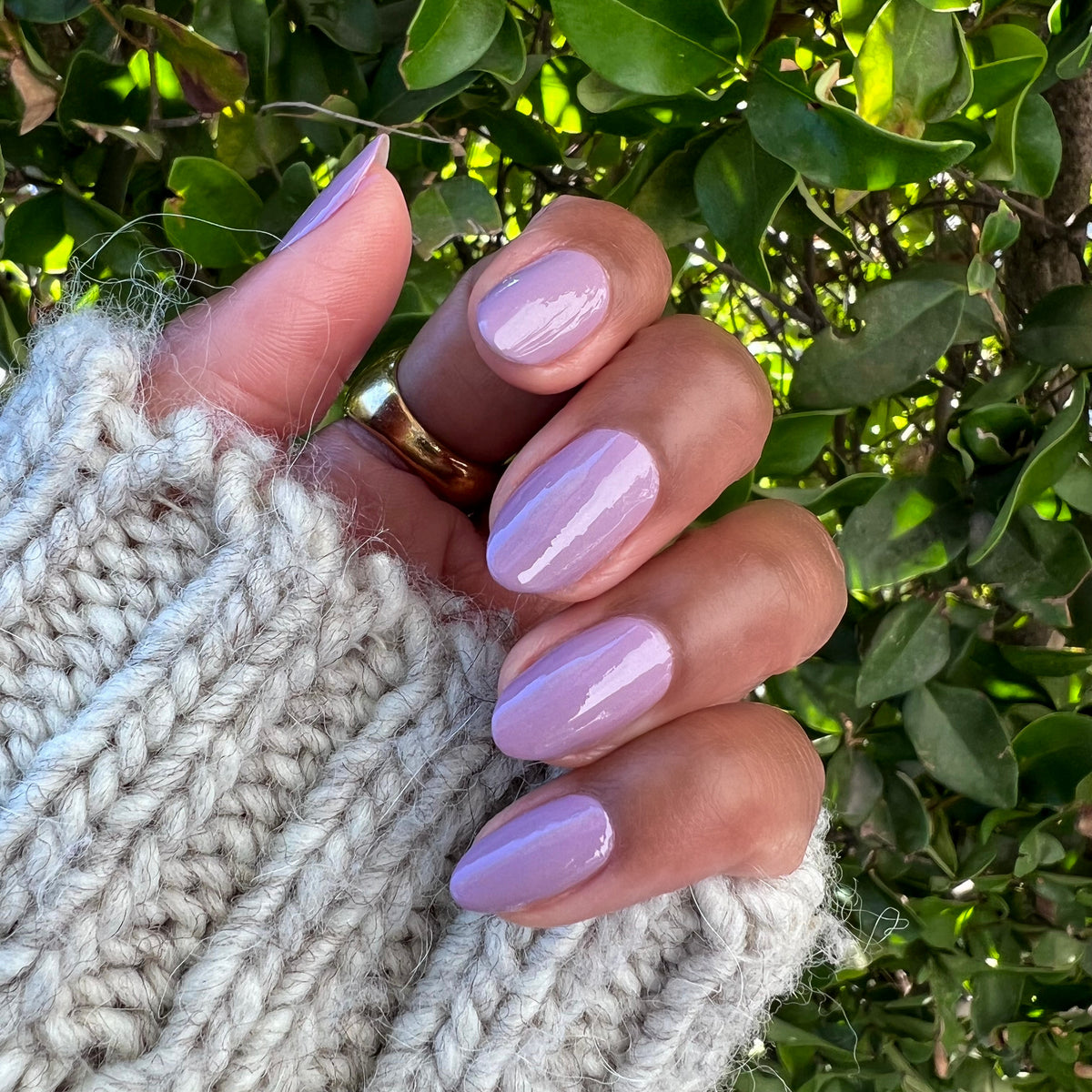 Hand with nails painted in glossy Prairie polish showing a soft blooming purple manicure by Olive and June