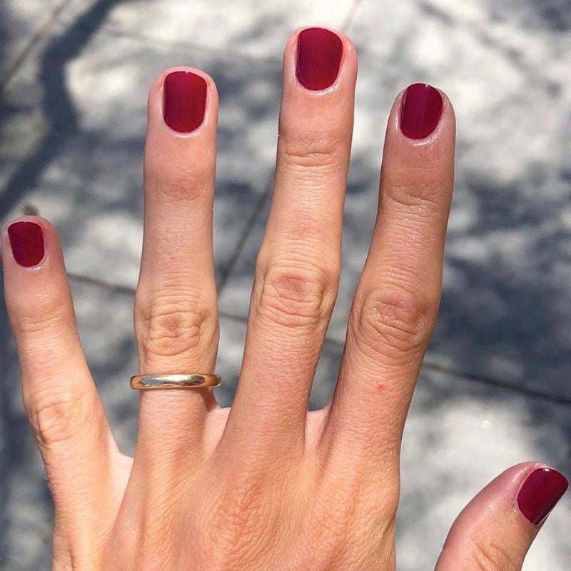 Hand with nails coated in SC deep bordeaux polish showing a sleek manicure under natural sunlight outdoors