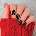 Hand with short nails painted shiny black polish wearing a vibrant red knitted sweater sleeve against gray fabric background thumbnail