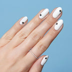 Hand with white polish and single black star nail stickers on each nail for Stars manicure against blue background