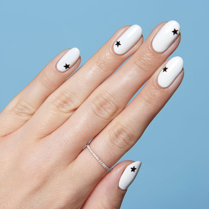 Hand with white polish and single black star nail stickers on each nail for Stars manicure against blue background
