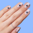 Hand with Stars manicure featuring pale pink polish and black star nail stickers on each nail against blue background