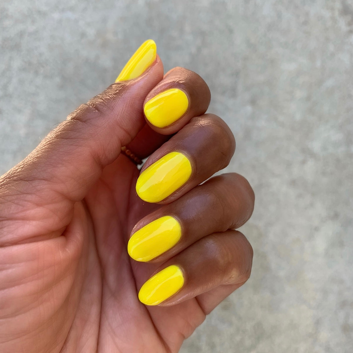 Hand with nails painted in bright Lemony Lemon polish showing glossy yellow manicure on natural background