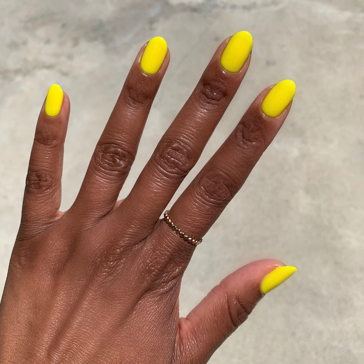 Hand with nails coated in bright Lemony Lemon polish wearing delicate gold ring on neutral background