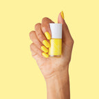 Hand holding bottle of Lemony Lemon yellow nail polish with matching bright mani against yellow background