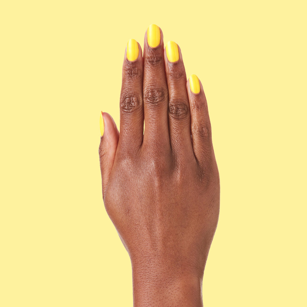 Hand with nails painted in bright neon yellow Lemony Lemon polish by Olive and June against yellow background