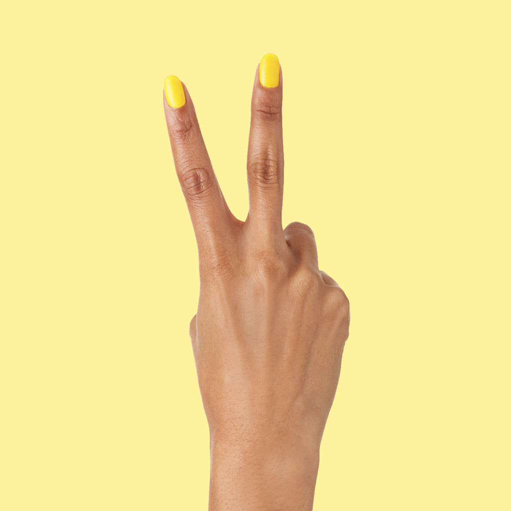 Hand with nails painted vibrant Lemony Lemon polish by Olive and June against bright yellow background