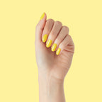 Hand showing nails painted in bright Lemony Lemon polish by Olive and June against pale yellow background