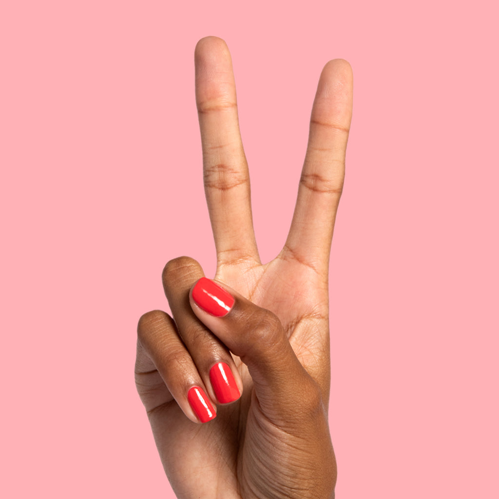 Hand showing peace sign with nails painted in bright orangey red Picante polish on smooth pink background for mani display