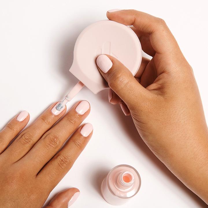 Hand using The Poppy universal polish handle to apply light pink nail polish for easier at-home mani control