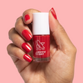 Hand holding a bottle of Smooch quick dry nail polish with matching red painted nails on pink background
