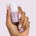 Hand with almond-shaped nails painted in glossy Purple Puka gel polish holding bottle of milky lavender iridescent polish