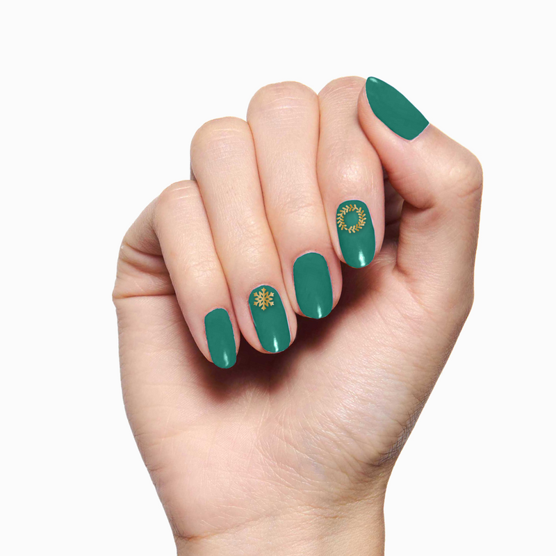 Hand with green polish and gold snowflake and wreath designs using O&J Cozy Lodge Nail Art Stickers for winter mani