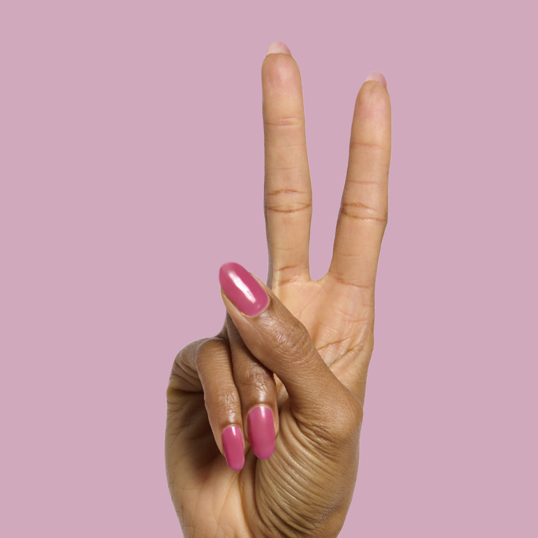 Hand with medium-length nails painted in This Lettuce is Radicchio magenta-purple polish against a pink background