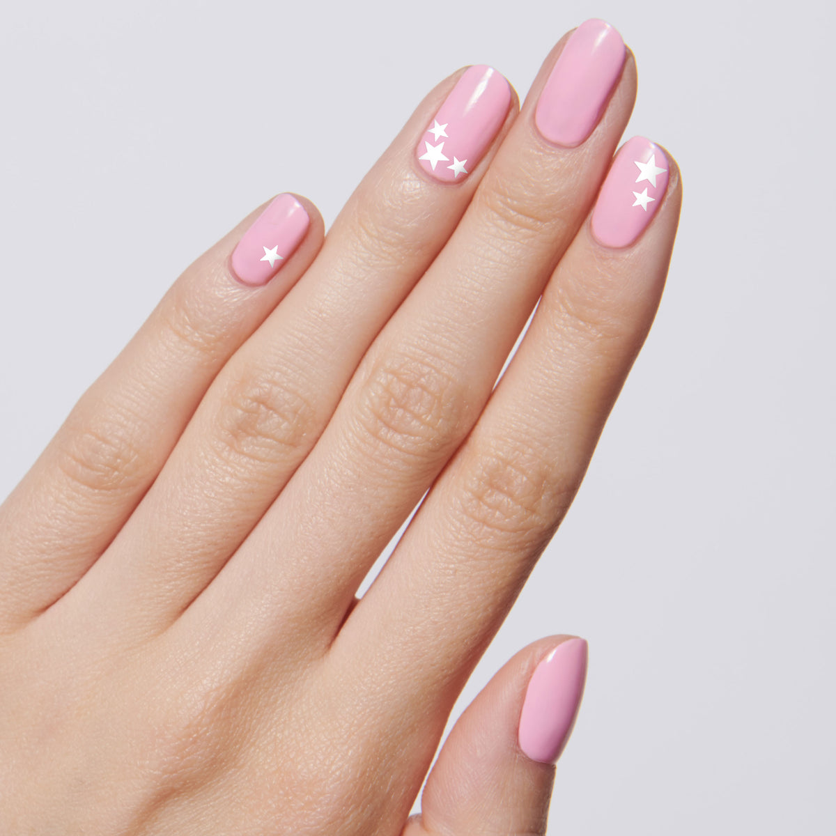 Hand with pink polish featuring white star nail stickers arranged on three fingers for Stars manicure
