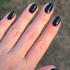 Hand with medium-length nails painted in glossy Cateye black polish showing a shiny at-home mani outdoors