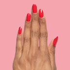 Hand with nails painted in glossy cherry red Lollipop quick dry polish against a soft pink background