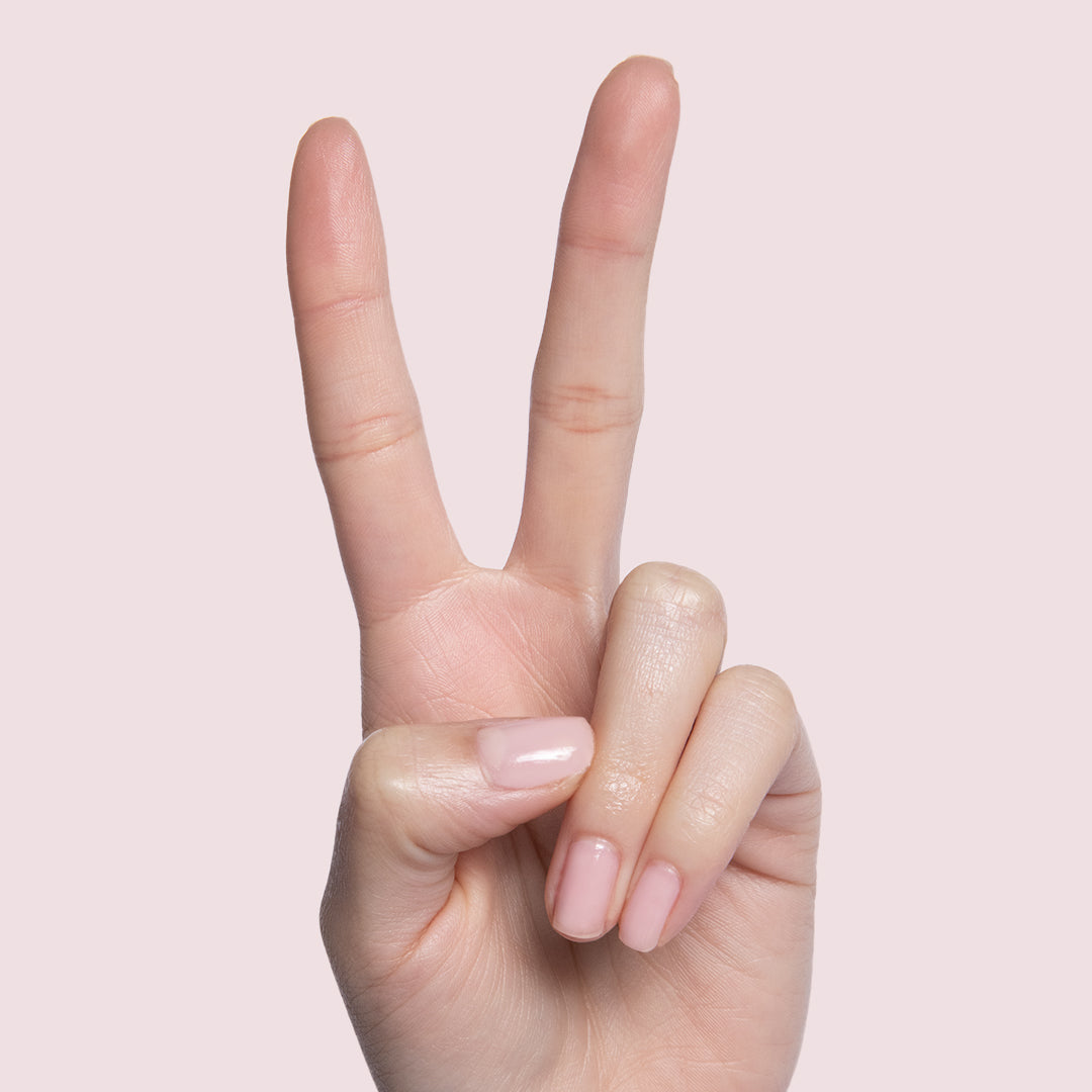 Hand showing peace sign with nails coated in Potpourri sheer mauve quick dry gel polish on soft pink background