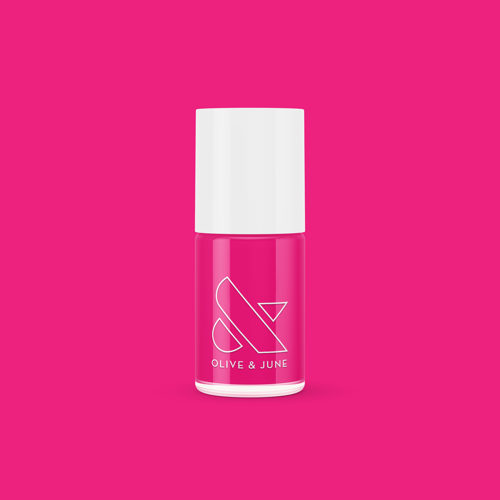 Bottle of Olive and June WILD ORCHID nail polish in rich magenta purple against a vibrant pink background